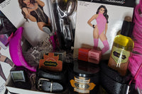 Adult goodie box with body oil, lingerie, handcuffs, vibrating underwear, body candle, love dice, body chocolate, thigh highs, & vibrator