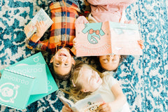 Two children reading books from Bookroo's Tween Book Club subscription on a colorful rug with additional books nearby