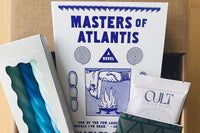 December 2023 box: Masters of Atlantis by Charles Portis. Contains "Cult" sea salt chocolate, spiral candles, and letterpress notebook.