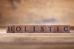 light brown blurred background with a sharp image of blocks, Each block has a letter and the entire word spells HOLISTIC.