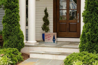 Gnome of the Month Club subscription box displayed on a front porch surrounded by neatly trimmed bushes
