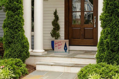 Gnome of the Month Club subscription box displayed on a front porch surrounded by neatly trimmed bushes