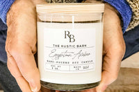 Hands holding a jar candle made of soy with the scent of Egyptian Amber from the Rustic Barn subscription box.