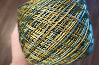 A Skein of Hand Dyed Silk Yarn in Sock Weight that has been wound into a cake with shades of green and yellow 