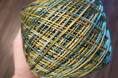 A Skein of Hand Dyed Silk Yarn in Sock Weight that has been wound into a cake with shades of green and yellow 