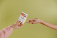 Pictured is a person's hand holding a small box containing Besti's self care collection as another hand reaches out for it.  