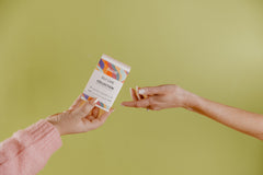Pictured is a person's hand holding a small box containing Besti's self care collection as another hand reaches out for it.  