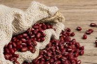 A hemp sprouting bag sits on a wooden background with red adzuki beans spilling out, ready to be sprouted.