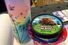 A tall sublimated mug with straw. The design is pastel colors and dandelions and butterflies with a hand sewn ice cream cozy. 