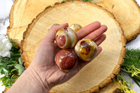 A photo of a hand holding three mookaite spheres as an example of a crystal of the month offered by Soul Gifts Crystals.