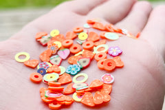Open palm holding clay hearts with the word love, clay circles that look like peach ring candies, Teal flowers, Pink flowers, and glitter