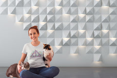 A woman sitting on the floor holding 2 cats and wearing a Deathly Hallows Tshirt with a purple triangle design.
