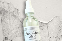 A bottle of the Coconut Hair Shine Mist by Greenmade goods with grey and white speckled concrete in the background.