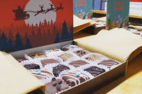 Image of an open Christmas-themed box of brownie bites. The Chrismas box includes a background image showing Santa;'s sleigh across a moon.
