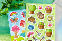 A green, springlike background featuring two sticker sheets - one with cute garden tools and another with mushrooms and fairies. 
