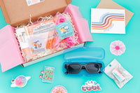 A summer-themed subscription box. Items include sunglasses in case, surf wax tin of chapstick, summer greeting card, surf van air freshener.
