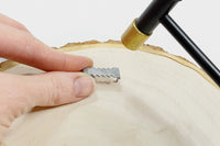Hand holding a sawtooth hanger on back of a project. Small metal hammer on the right comes with the Woodburning Tools and Accessories Kit.