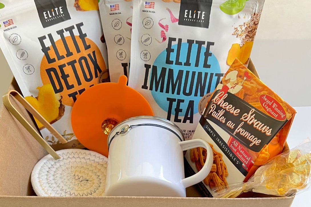 Elite positiviTea box with organic herbals supports immune and digestive systems. Elite tea box has a cup, lid, placemate, snack, honey