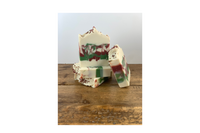 Stack of Applewood Fir Needle soap on a wooden table with white background. The soap is swirled in green, red and cream colors.