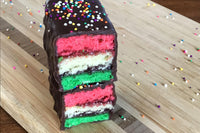 Nettie's Craft Brownies rainbow cookies sprinkles chocolate dipped side view of stacked cookies on cutting board.