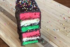 Nettie's Craft Brownies rainbow cookies sprinkles chocolate dipped side view of stacked cookies on cutting board.