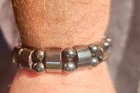 A dark silver bracelet on a wrist. The beads are two circular beads stacked between two longer rectangle beads.