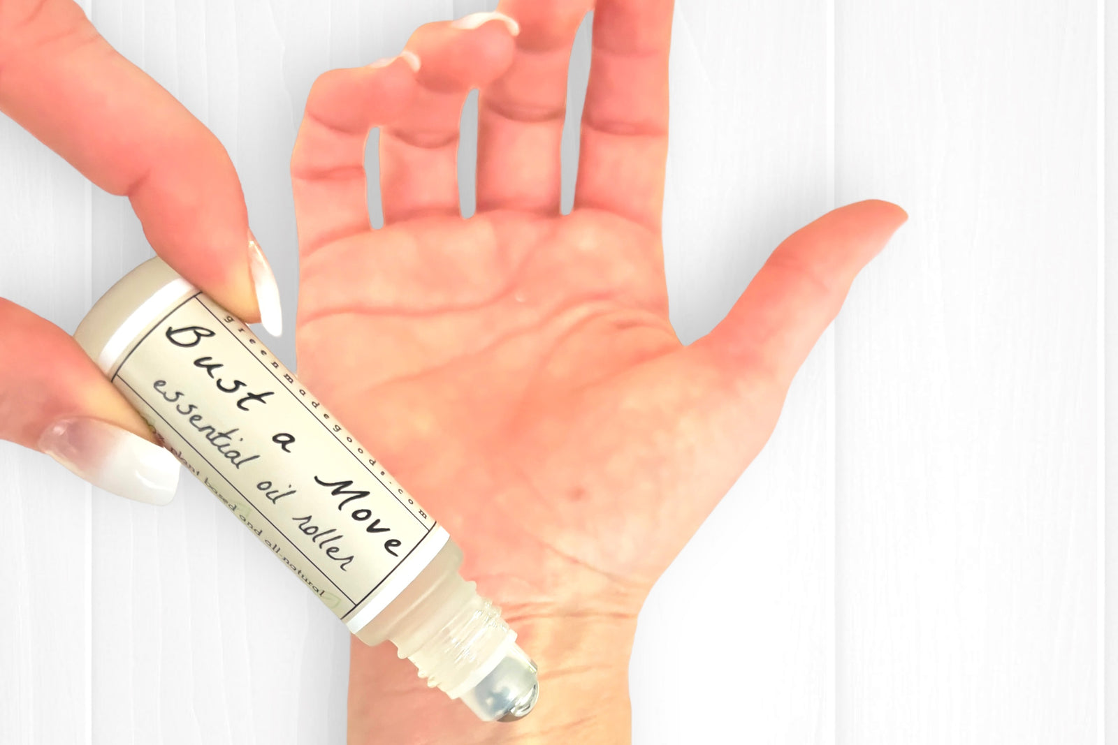 Woman's hands with natural french nails applying the Bust a Move Essential Oil Roller to her right wrist.