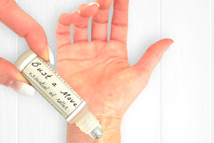 Woman's hands with natural french nails applying the Bust a Move Essential Oil Roller to her right wrist.