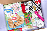 Contents of a 90s-themed subscription box. Items include funky socks, scrunchie, furby enamel pin, and a blockbuster magnet.