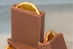 Orange Patcholi bars of soap stacked on top of each other with a bar leaning on the stack. Each has a dried orange slice for decorative top.