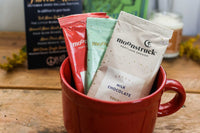 A red mug filled with three packets of Moonstruck milk chocolate, featured in the Peace & Pages monthly subscription box