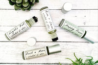 Four essential oil rollers on white washed wood with plants. Lights Out, Rise + Shine, Happy Place, and Bust a Move.