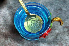 A blue shimmer tea colored with herbs with blue shimmer floating in the cup. One of my gold spoons sits in the cup.