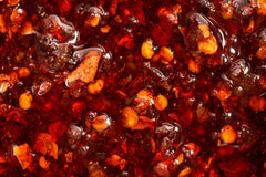 A blown up shot showing the crunchy and delicious flavors of chili crisp, floating around in oil. Garlic and chilis for days