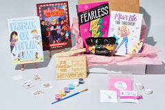 An open Between the Bookends subscription box filled with books for tweens, paints and jewelry. Full size version pictured.