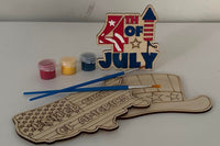 Three wooden patriotic shapes with 2 paint brushes and a paint sampler. One of the shapes is painted as an example.