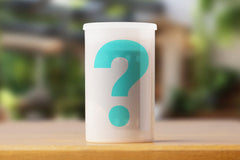 A semi transparent film roll container with a teal question mark, indicating it is a mystery roll of expired film