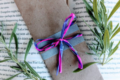 A fantasy romance-themed bookmark wrapped in brown craft paper and adorned with pink and purple ribbons rests on an open book.