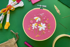 embroidery project featuring three daffodils on pink fabric, surrounded by colorful embroidery kit supplies