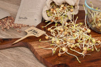 Pea sprouts are sprawling out of a hemp sprouting bag onto a wooden chopping board. A Sproutie seed packet is in the background.