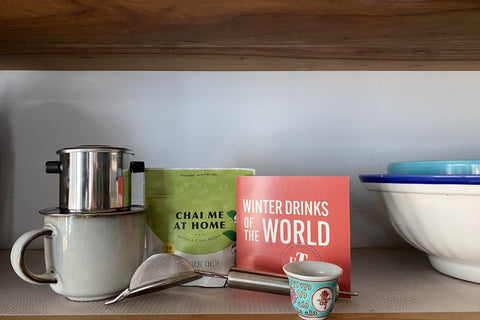 Photograph includes a Vietnamese coffee phin, a package of chai, a winter drinks of the world recipe booklet and a Chinese wine cup