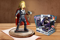 A Sculpted Thor Figurine holding his iconic hammer and a deck of Avengers Playing cards sitting on a wooden table.