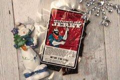 A single bag of House of Jerky Chipotle Bourbon jerky.  On a white barn wood background with a snowman and snowflake.