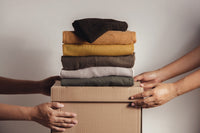 Two sets of hards are pictured. They are both holding a cardboard box with six pieces of clothing folded on top of it. 