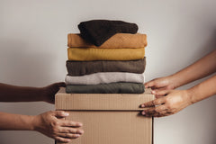 Two sets of hards are pictured. They are both holding a cardboard box with six pieces of clothing folded on top of it. 