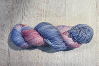 Close up photo of a hand dyed skein of sock weight yarn against a solid background. The skein is twisted and shows a variety of color.
