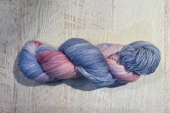 Close up photo of a hand dyed skein of sock weight yarn against a solid background. The skein is twisted and shows a variety of color.