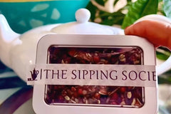 The Sipping Societea Loose leaf tea subscription box with tea tin in front of a decorative tea pot ready to be brewed.