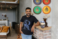 Man wearing a Letter R Ravenclaw Tshirt with a Dumbledore mug by him and 4 House Wall plates on the wall.