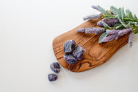 white background with light brown wood tray. raw and rough purple stones on the board and the white background as if spilling off. 